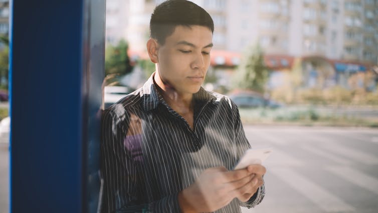 a young man in a leather jacket looks at his phone while waiting for the bus