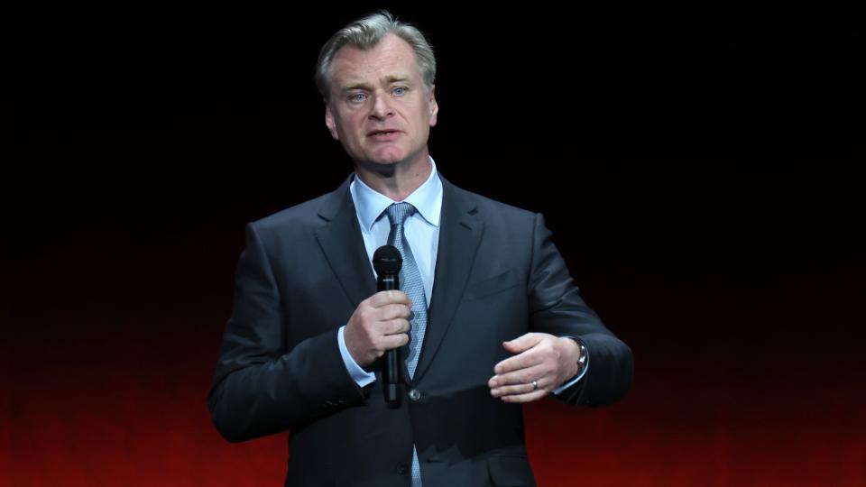 Christopher Nolan speaking on stage and holding a microphone while promoting his film "Oppenheimer"  at CinemaCon in Las Vegas