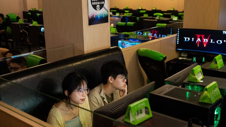 A photo showing a young couple sitting together in an internet cafe with green and black chairs.